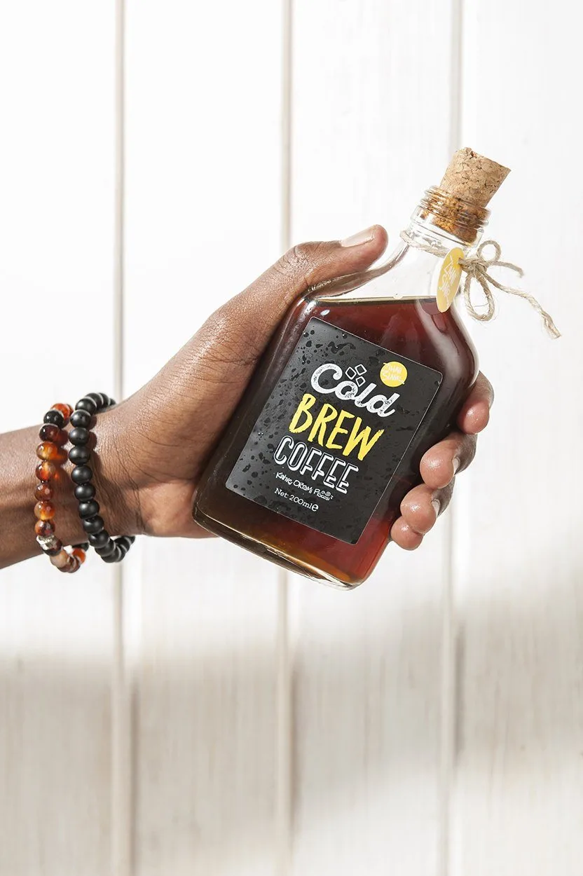 Elde tutulan cold brew kahve şişesi, beyaz ahşap zemin üzerinde ürün fotoğrafı