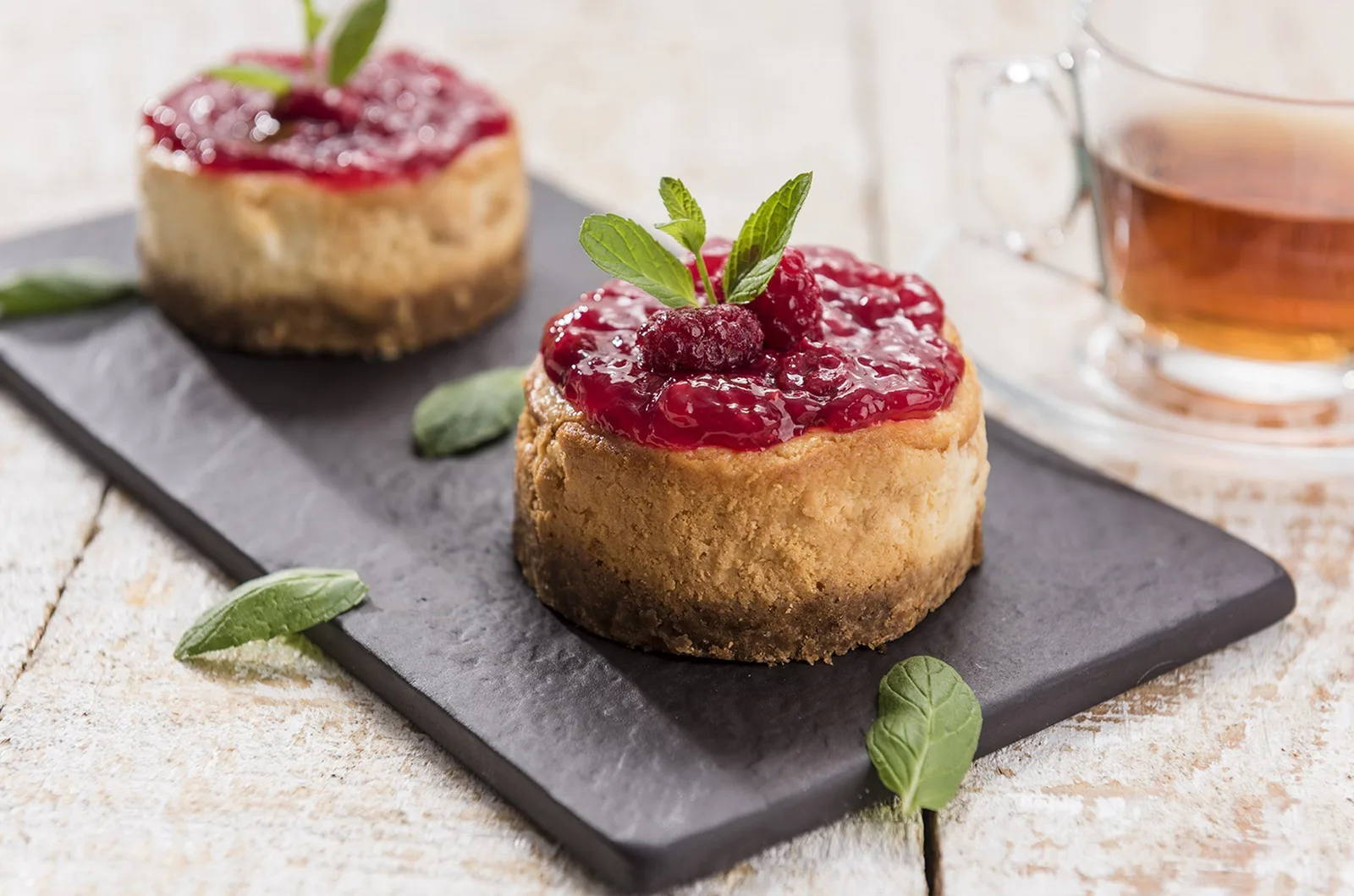 Kara taş tabak üzerinde frambuazlı mini cheesecake'ler ve çay, tatlı fotoğrafı