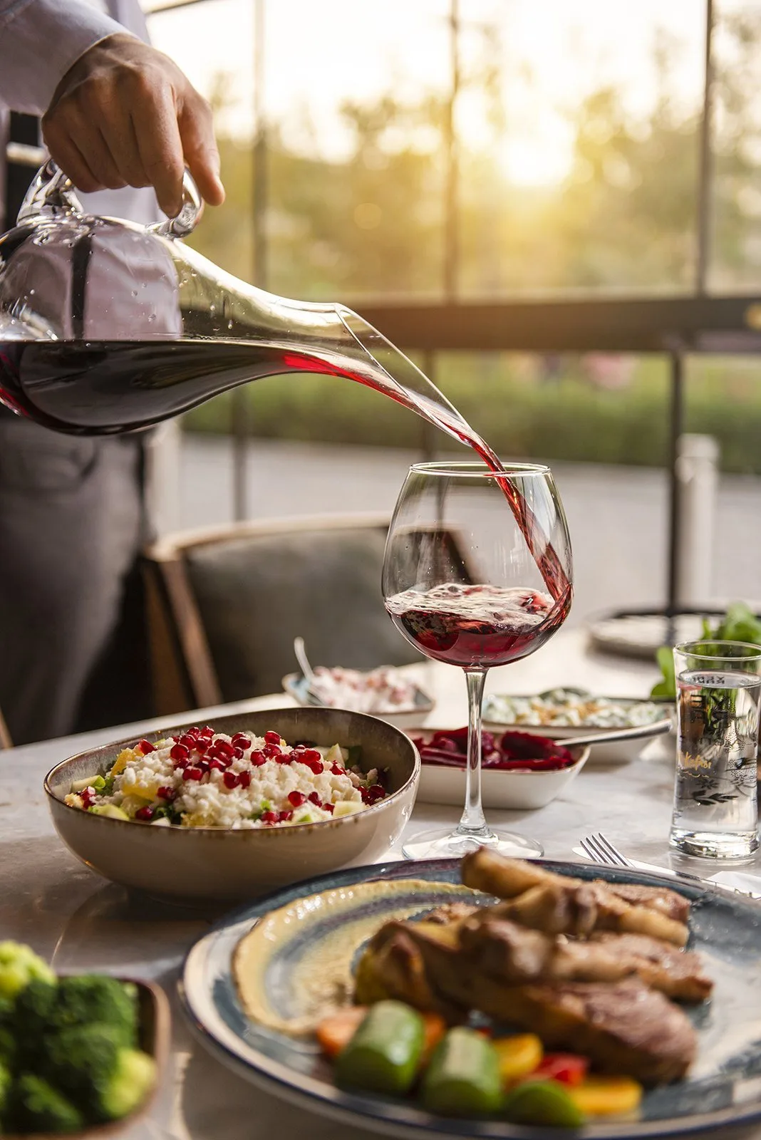 Restoran masasında karafa dökülen kırmızı şarap ve yemekler, mekân fotoğrafı