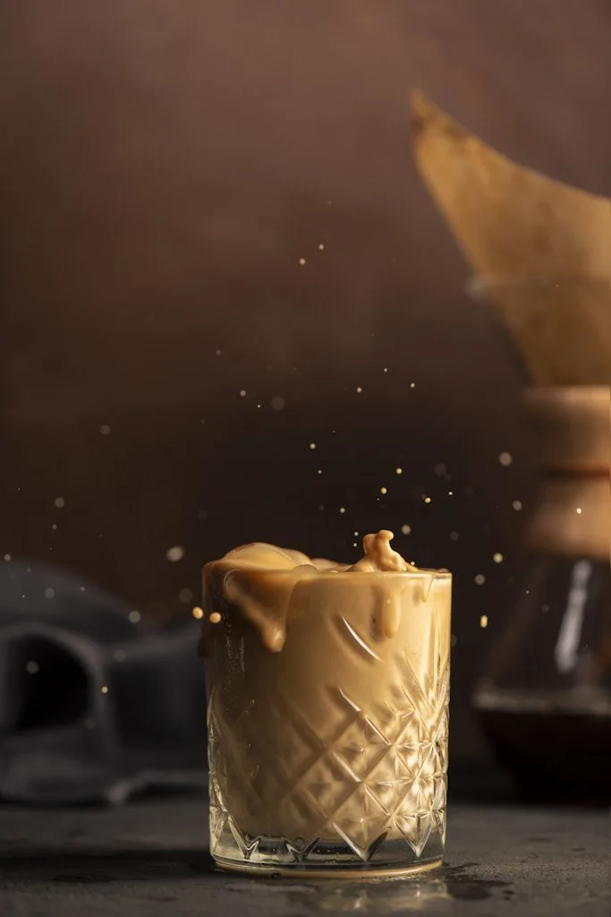 Kristal bardakta sıçrayan buzlu kahve, koyu zemin hareketli içecek fotoğrafı